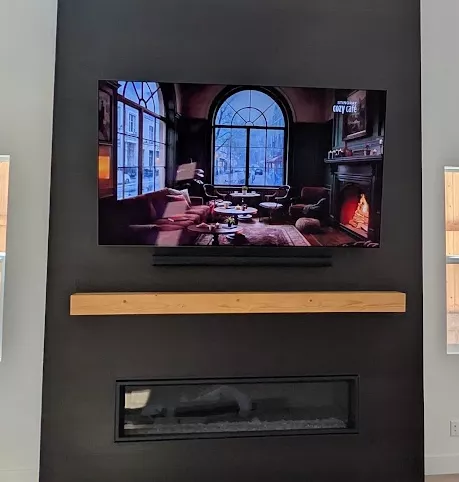 TV and soundbar mounted on a dark feature wall above a wood mantel and linear fireplace