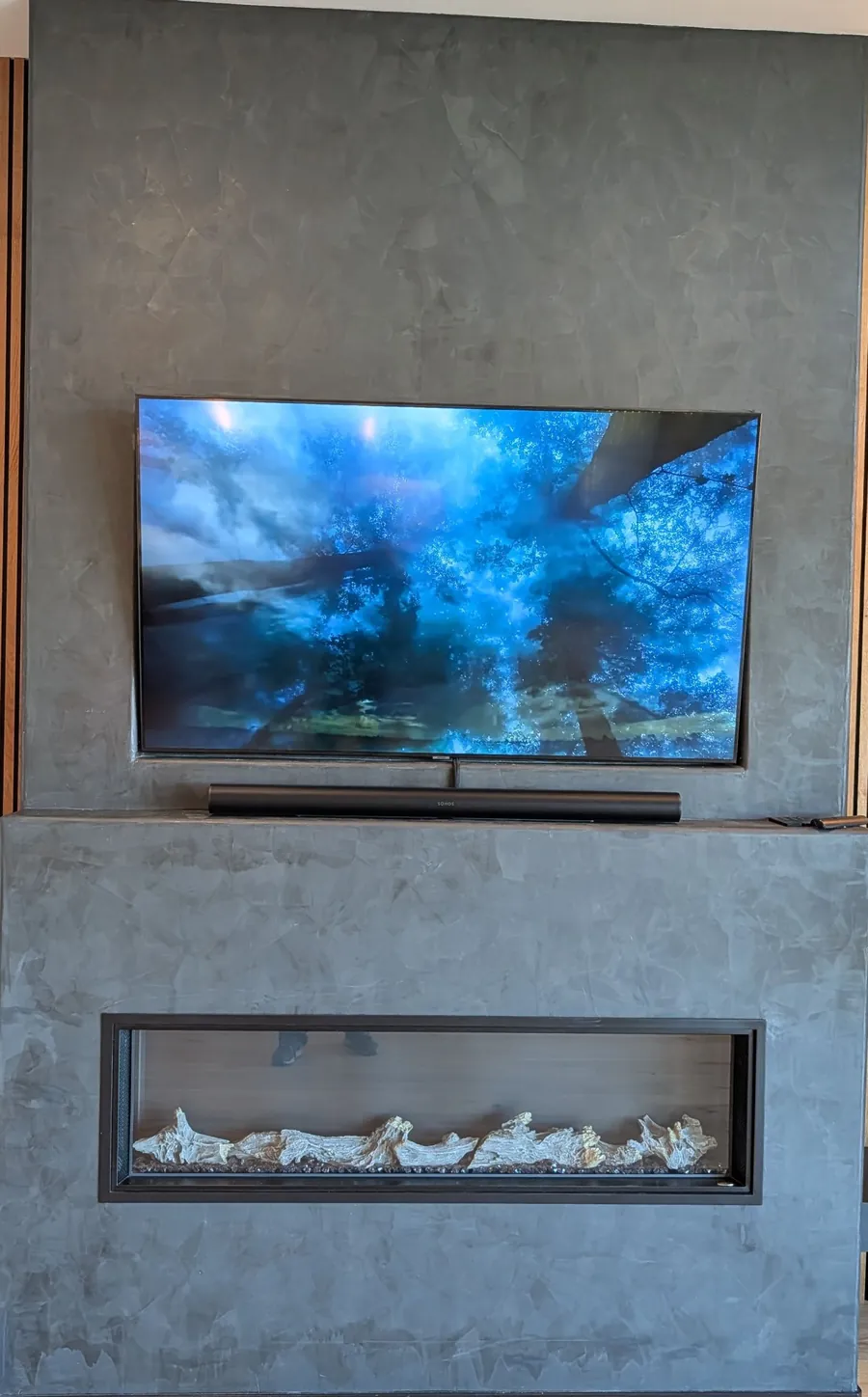 TV mounted on a textured grey feature wall above a linear fireplace, with a soundbar on the mantel